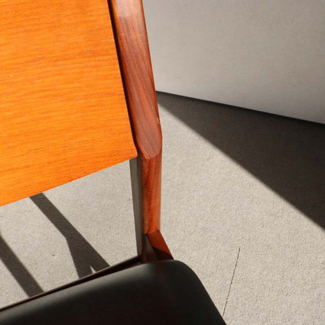 Mid-century British vintage dining chair with sleek teak wood frame and black leather seat, showing rich wood grain and.