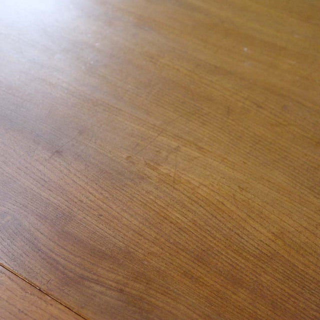 Close-up of vintage British mid-century teak dining table surface showing smooth wood grain and warm honey tones.