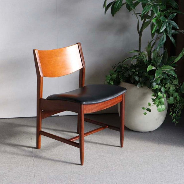 Mid-century British vintage teak dining chair with rich wood grain and black leather seat cushion, sturdy angled legs, and.