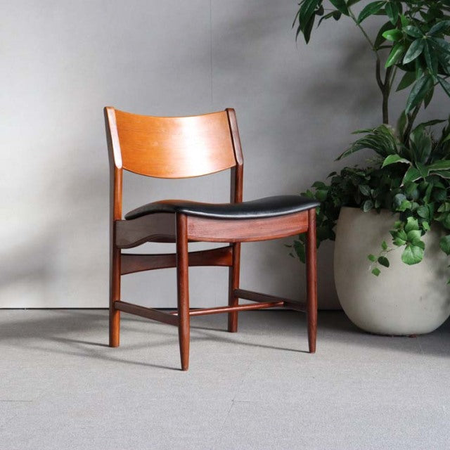 Mid-century British vintage teak dining chair with curved backrest and black leather seat, smooth wood grain and tapered legs.