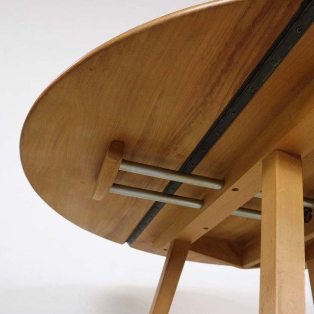 Mid-century British vintage Ercol dining table in teak with circular drop-leaf top and slender angled legs showing warm wood .