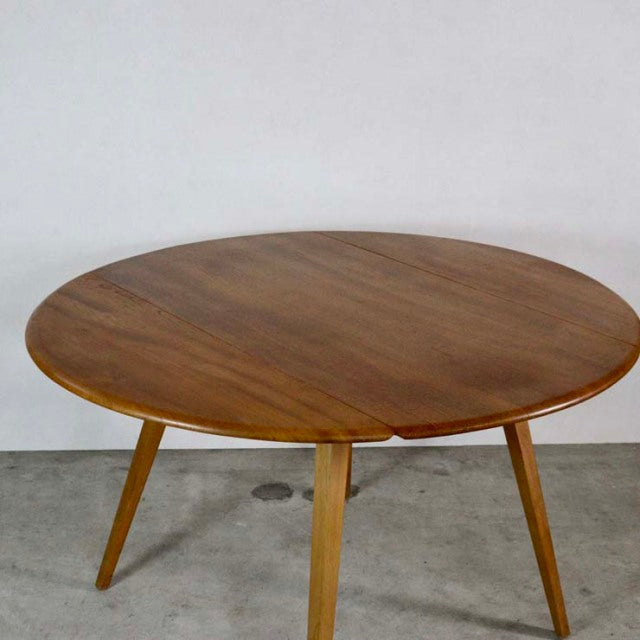 Vintage mid-century British Ercol dining table in teak with round drop-leaf top and angled legs.
