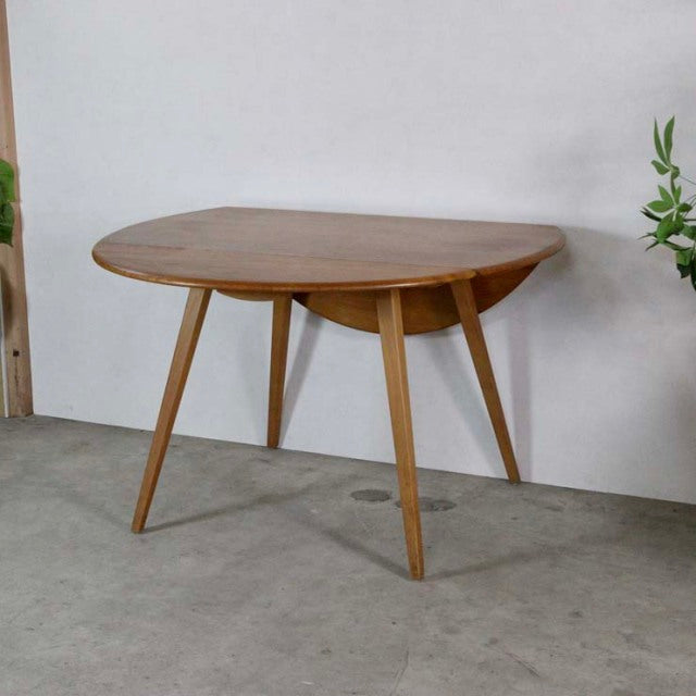 Vintage British mid-century Ercol teak drop-leaf dining table with rounded top and tapered legs.