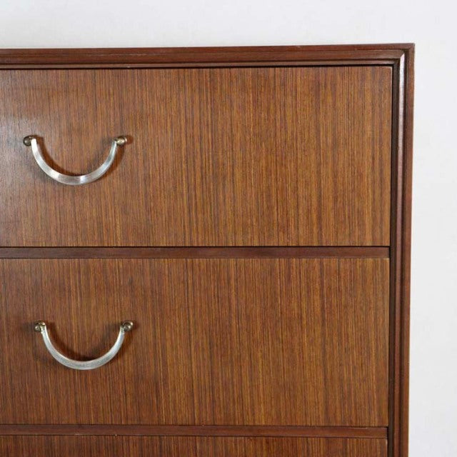 Mid-century British vintage teak chest with six smooth drawers and curved metal handles, showcasing rich wood grain and.