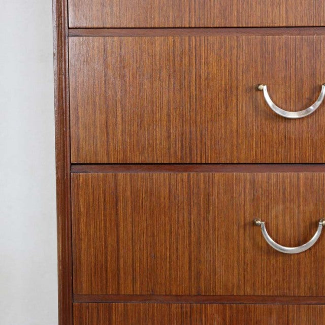 Vintage British mid-century teak chest with six drawers, smooth wood grain, and curved metal handles.