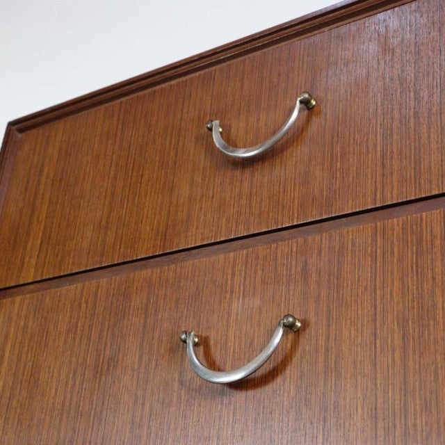 Close-up of vintage British teak mid-century chest drawers with curved metal handles and fine wood grain texture.
