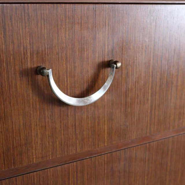Close-up of vintage teak drawer with curved brass handle on British mid-century chest.