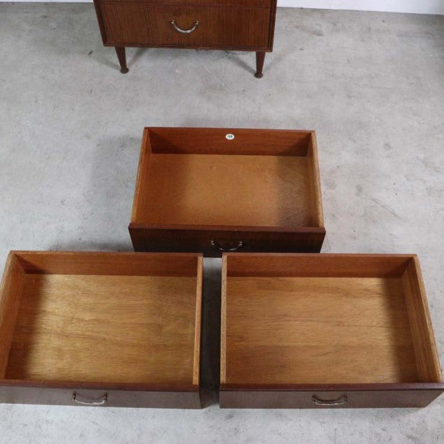 Mid-century British vintage teak chest of drawers with visible wood grain and slender tapered legs, drawer interiors showing .