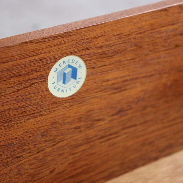 Close-up of vintage teak wood grain with circular Meredew Furniture British brand label on mid-century Denmark chest drawer.