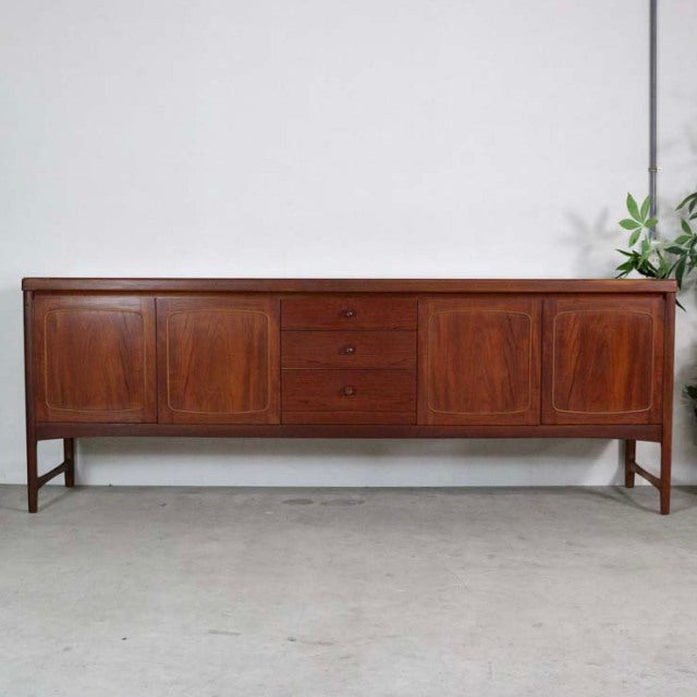 Mid-century British vintage teak sideboard by Nathan with rich wood grain, three central drawers, and flanking cabinet doors .