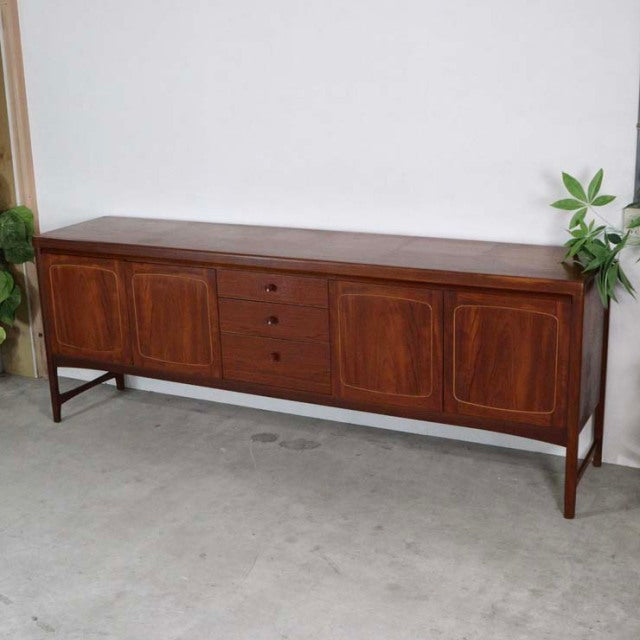 Mid-century British vintage teak sideboard by Nathan with rich wood grain, four cabinet doors, and three central drawers on.