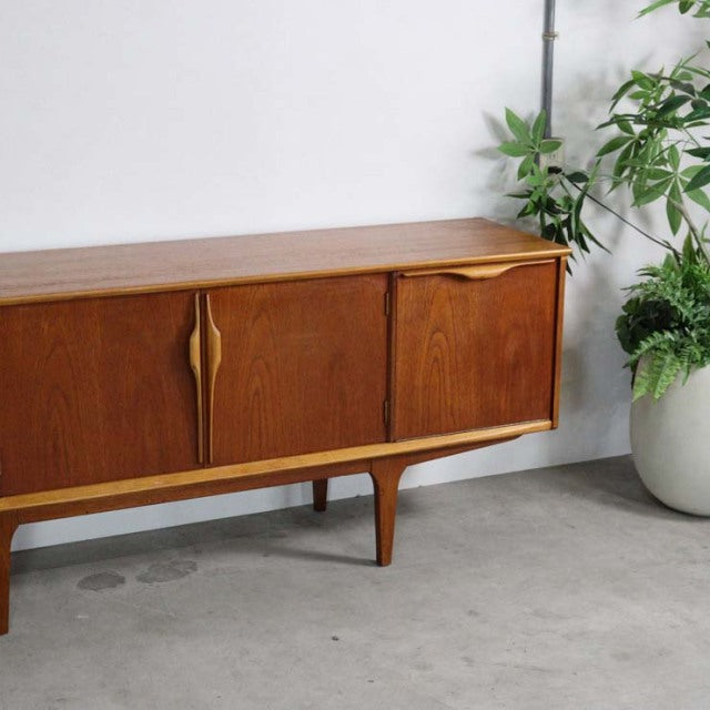 Mid-century British vintage teak sideboard with smooth wood grain, sculpted handles, and slender tapered legs from Jentique.