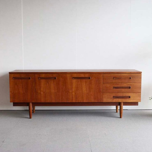 Mid-century vintage teak sideboard with smooth wood grain, British-Denmark design, featuring three drawers and two cabinets.