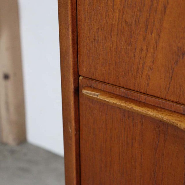 Mid-century British teak sideboard with warm grain, smooth curved wooden handle, and clean lines.