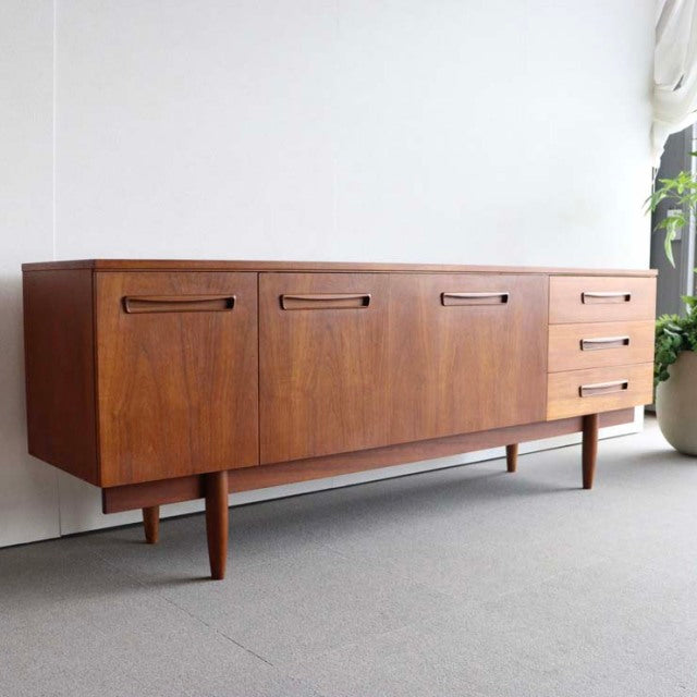 Vintage teak sideboard with smooth wood grain, clean mid-century British design, tapered legs, and three drawers on the.