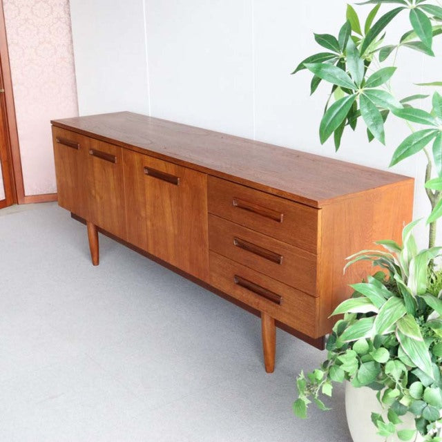 Mid-century vintage teak sideboard with rich wood grain, tapered legs, three drawers, and dual cabinet doors,.