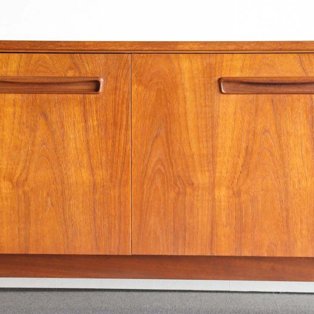Mid-century vintage teak sideboard with rich wood grain, sleek integrated handles, and smooth finish reflecting.