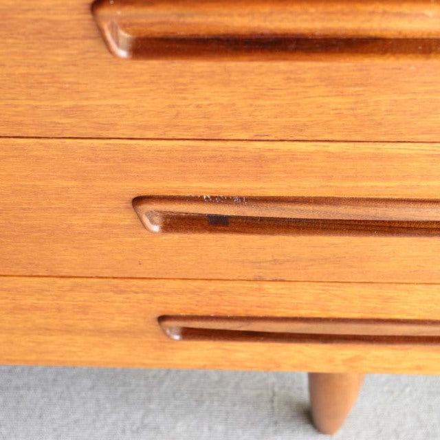 Close-up of vintage teak sideboard drawer handles with rich wood grain and tapered mid-century Danish legs.
