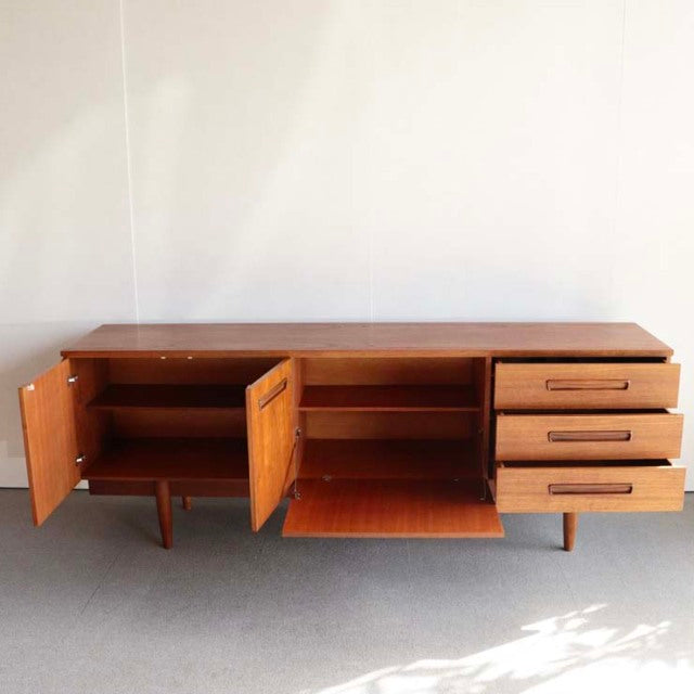 Mid-century vintage teak sideboard with British-Denmark design, featuring open double doors, three drawers, and tapered legs.