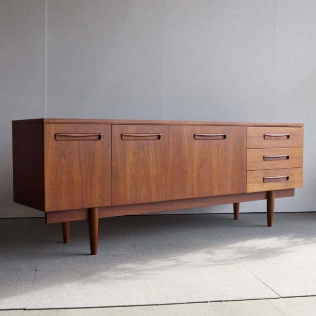Vintage teak sideboard with rich wood grain, clean British mid-century Denmark design, tapered legs, four drawers, and three .