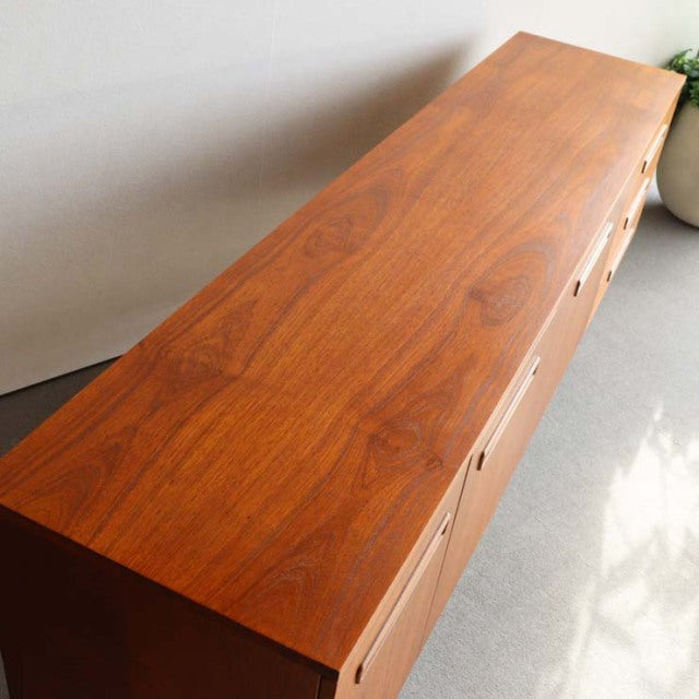 Long mid-century teak sideboard with rich wood grain, sleek British design, and slender angled legs.