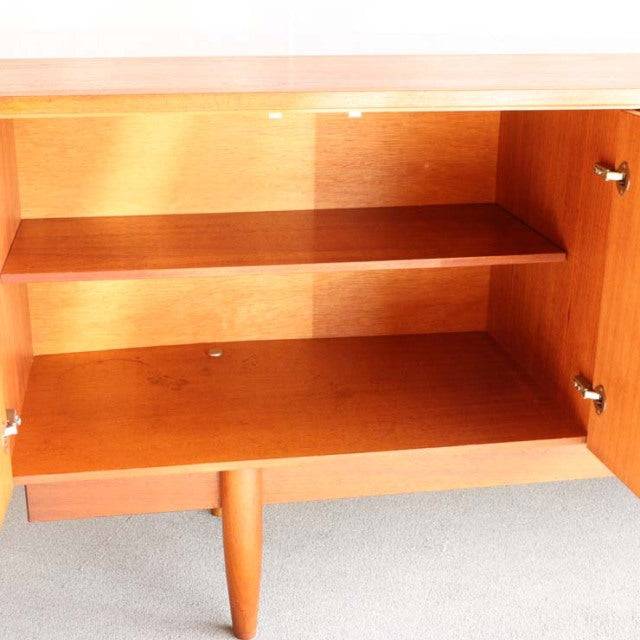 Open vintage teak sideboard door revealing rich wood grain interior and mid-century tapered legs.