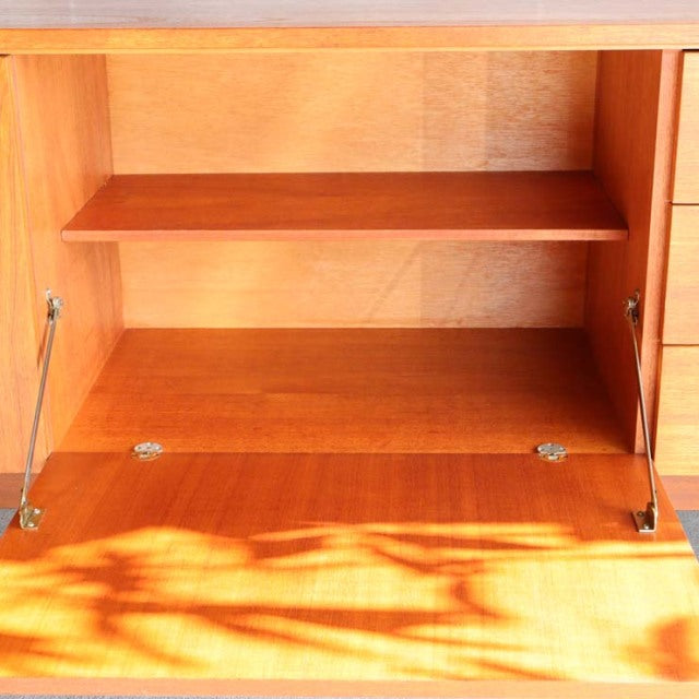 Mid-century teak sideboard cabinet open with visible wood grain and brass hardware, British-Denmark vintage style.