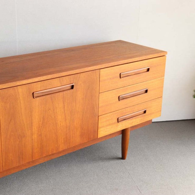 Vintage teak sideboard in mid-century British style with rich wood grain, tapered legs, and integrated handles.