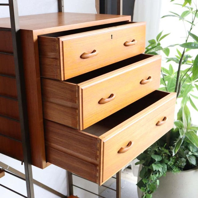 Vintage mid-century teak Ladderax shelving unit with three open drawers, showcasing rich wood grain and curved handles,.