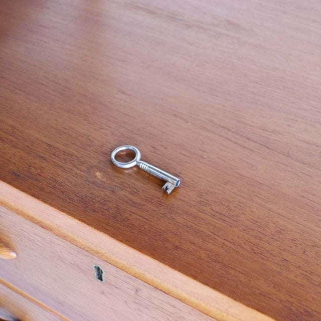 Vintage teak Ladderax unit shelf surface with smooth wood grain and small metal key, mid-century British-Denmark design.