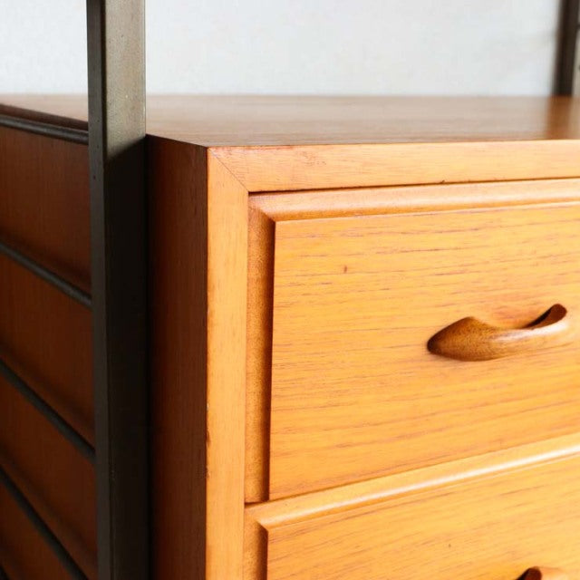 Mid-century British Ladderax unit shelf in vintage teak with smooth wood grain and rounded drawer handles, sleek black metal .