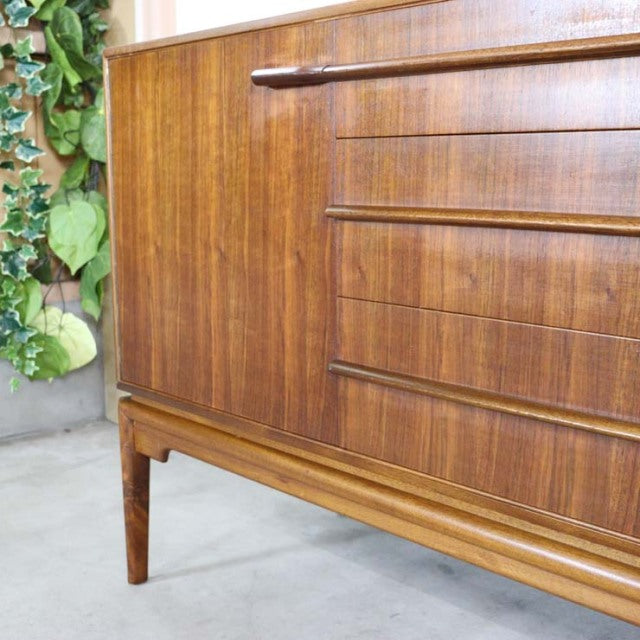 Vintage mid-century A.H.McIntosh teak sideboard with rich wood grain, sleek horizontal drawer handles, and tapered legs,.