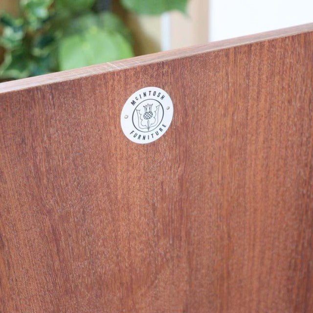 Close-up of teak wood grain and A.H. McIntosh British vintage mid-century label on sideboard panel.
