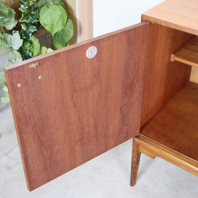 Mid-century British teak sideboard door with rich wood grain and brass fittings, legs visible at base.