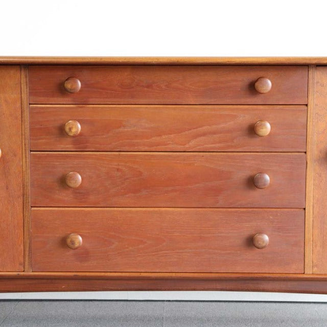 Vintage mid-century teak sideboard with British design, four drawers, round wooden handles, smooth wood grain, and tapered.