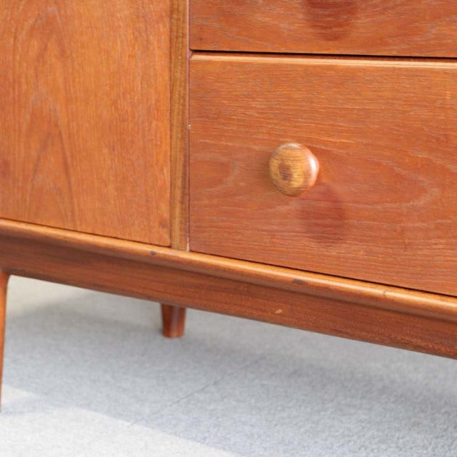 Mid-century teak sideboard corner with smooth wood grain, rounded wooden knob, and tapered British-style legs from Denmark.