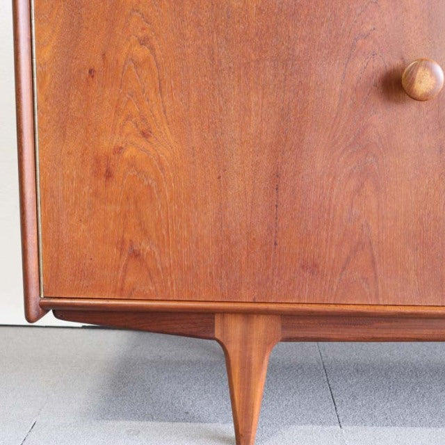 Vintage teak sideboard corner with smooth wood grain, tapered mid-century British legs, Danish design influence.