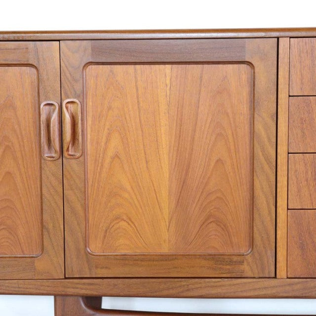 Vintage British mid-century teak sideboard with smooth wood grain, curved recessed door handles, and a warm natural finish.
