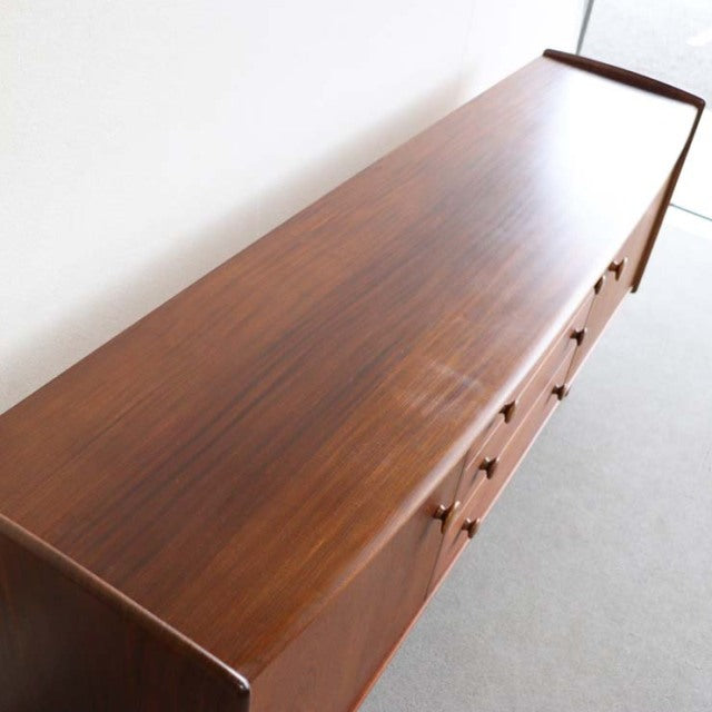 Vintage mid-century teak sideboard with smooth wood grain, British-Denmark design, tapered legs, and clean lines.