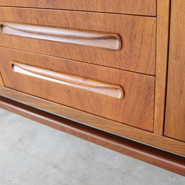 Vintage British mid-century teak sideboard with smooth wood grain, curved recessed handles, and sleek rounded legs.