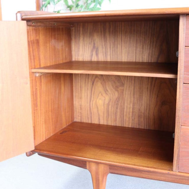 Vintage teak sideboard with British mid-century Denmark design, smooth wood grain and tapered legs, open cabinet view.