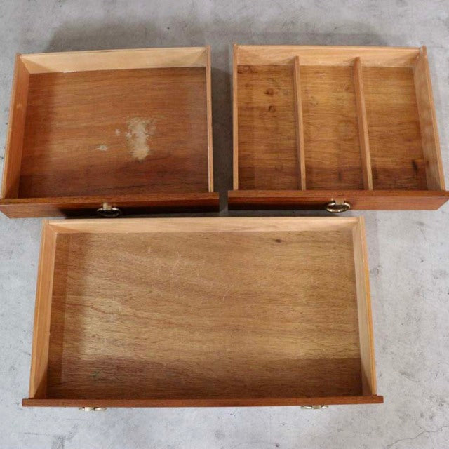 Three teak wood drawers with visible wood grain, brass handles, and a mid-century vintage British design.