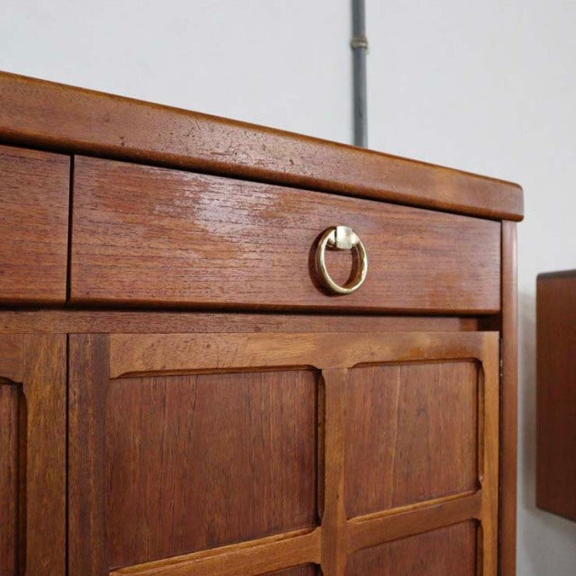 Vintage British Nathan teak sideboard with mid-century Denmark design, brass ring drawer pull, warm wood grain, and raised.