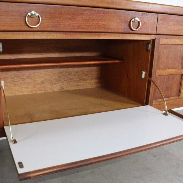 Mid-century British vintage teak sideboard by Nathan with open front drop-down door, brass hardware, and visible wood grain.