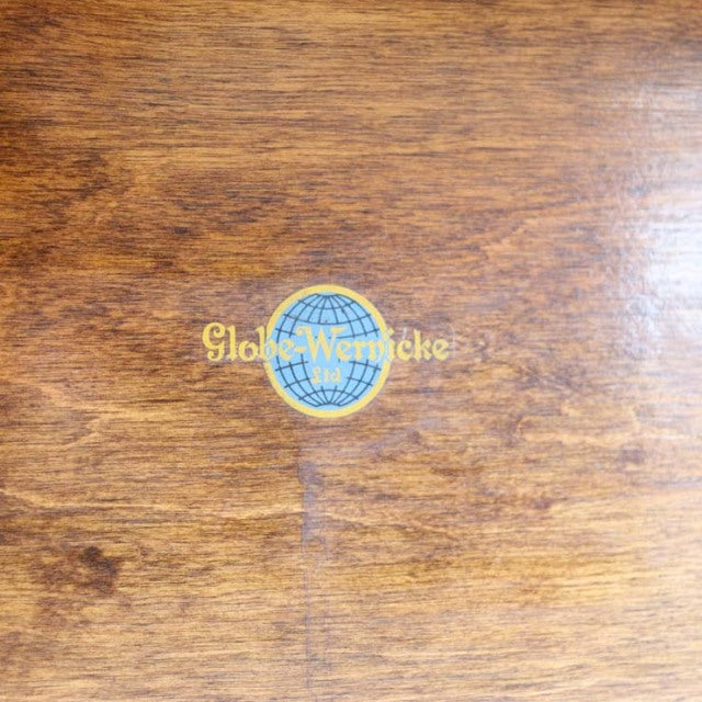 Close-up of vintage teak wood surface with Globe Wernicke British mid-century logo featuring a blue globe emblem and gold.