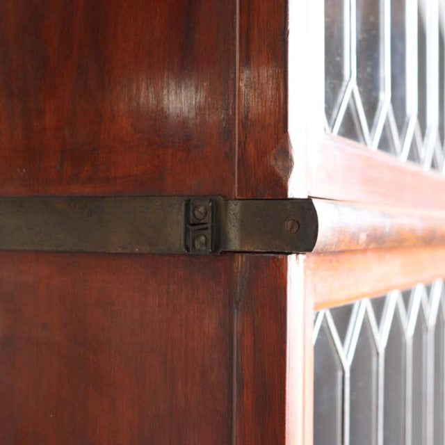 Close-up of vintage teak Globe Wernicke glass bookcase corner with metal strap and diamond-patterned glass, mid-century.