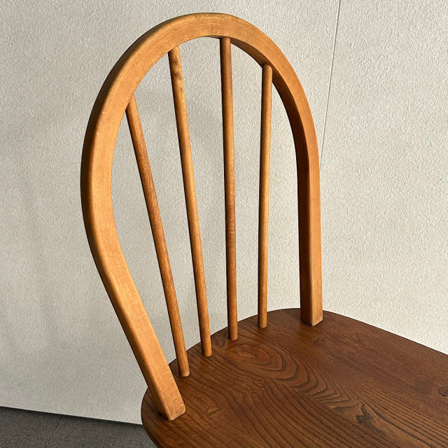 Mid-century British vintage Ercol hoop back chair in warm teak with curved spindled backrest and smooth wood grain seat.