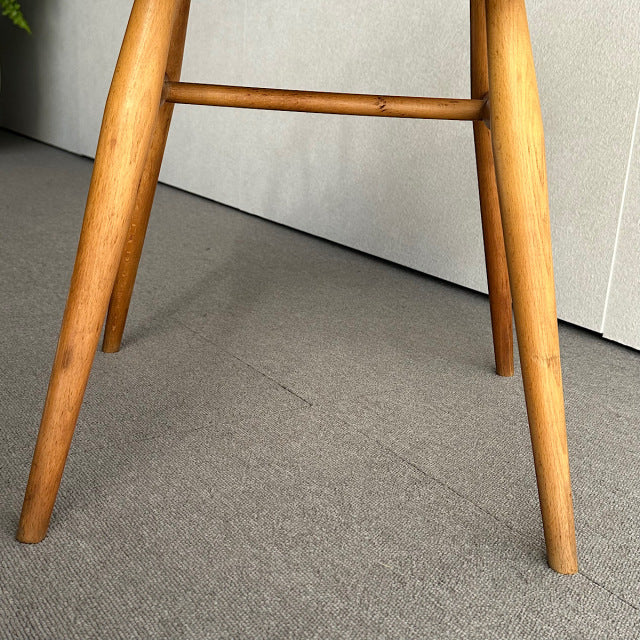 Close-up of mid-century British vintage Ercol hoop back chair legs in warm teak wood with visible grain and spindle.