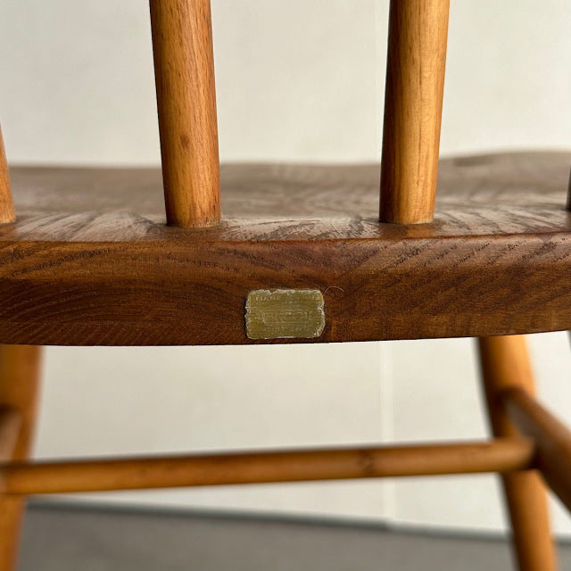 Close-up of vintage British mid-century teak wood chair frame with visible wood grain and brass label on horizontal support.