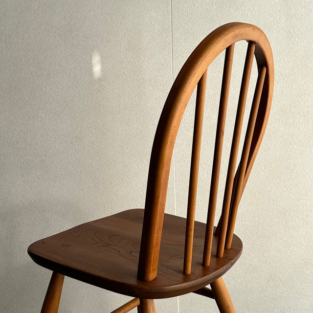 Mid-century British vintage Ercol hoop back chair in warm teak with curved spindle backrest and smooth wood grain finish.